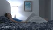 Woman laying on her back on the bed with a pillow under her knees.