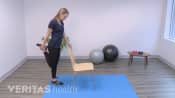 Woman standing behind a chair doing a standing quadricep stretch.