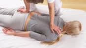 Massage therapist applying pressure to the upper back and buttocks of a person lying prone.