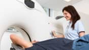 CT tech administering a CT scan to a patient lying prone with arms over their head.