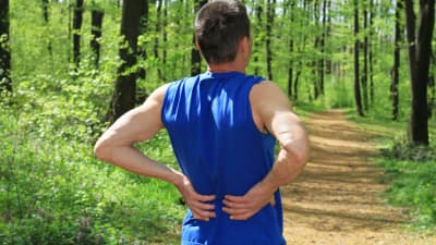 Man grasping lower back on running trail
