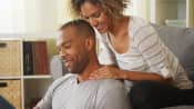 Young man with neck pain sitting on floor with woman on the couch