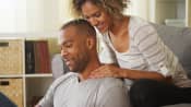 Young man with neck pain sitting on floor with woman on the couch