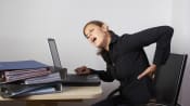 Professional woman grabbing her lower back with a pained look on her face