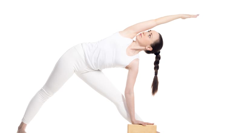 Woman performing the triangle yoga pose using a yoga block.