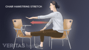 Profile woman sitting in a chair with foot up in another chair doing a hamstring stretch.
