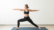 Woman performing the warrior 2 yoga pose on a yoga mat.